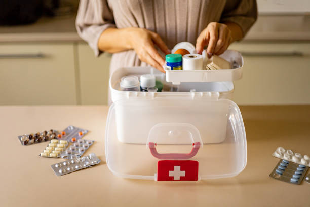 Closeup female hand neatly placing medicament at domestic first aid kit top view. Storage organization in transparent plastic box drug, pill, syringe, bandage. Fast health help safety emergency supply