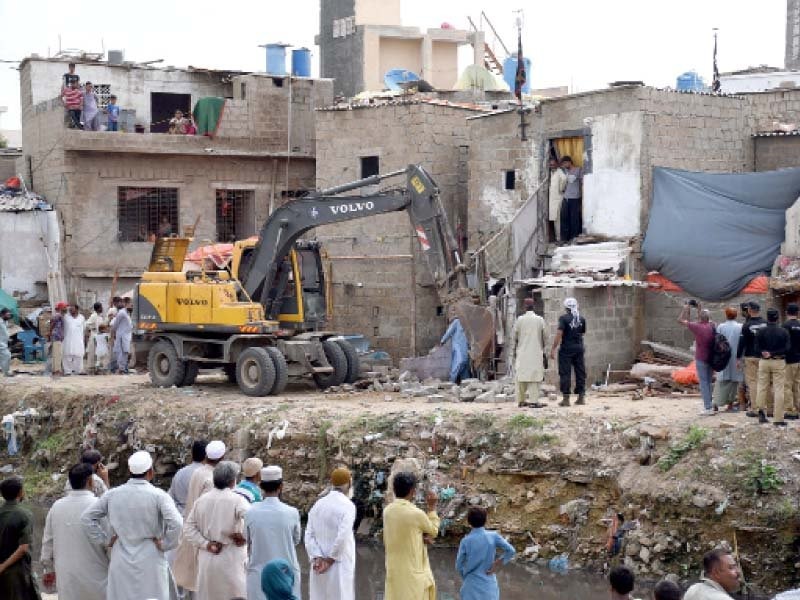 People stand on the side as a bulldozer demolishes houses during anti-encroachment campaign.