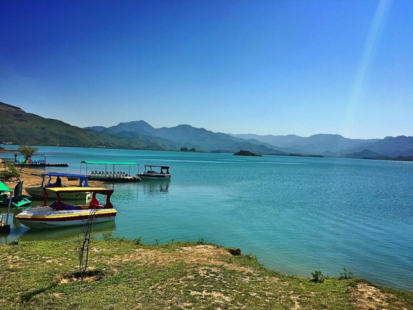 the view of Khanpur Dam with boats docked and the mountains in the background