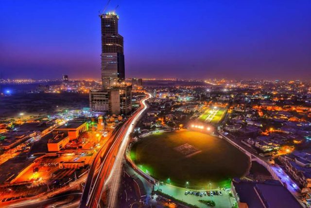 Night view of Bahria Icon Tower surrounded by a stadium, houses and other buildings