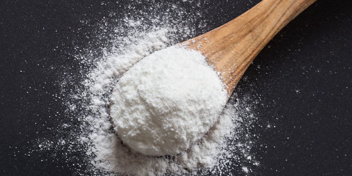 Baking soda on a wooden spoon on dark background, top view