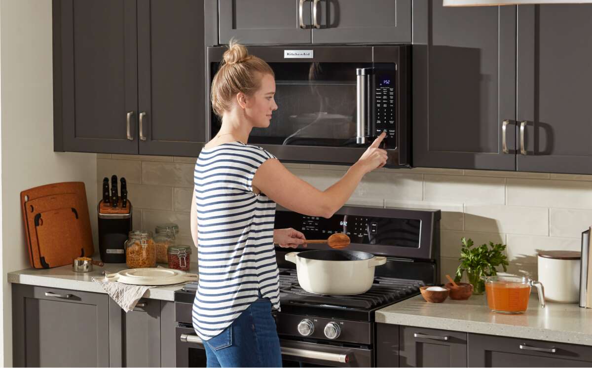 A woman cooking on a stove and using built in microwave