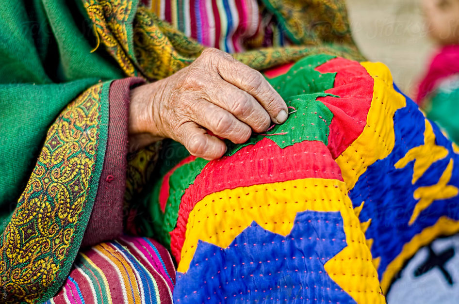 An old lady engaged in sewing a traditional quilt called Rillie.